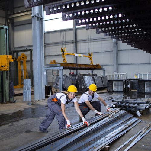 Factory workers handling metal parts together.
